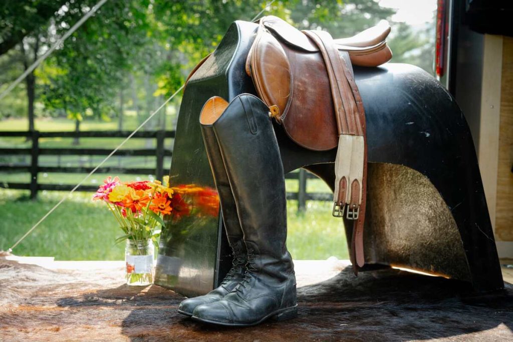 Saddle with girth, tall boots and jar of flowers